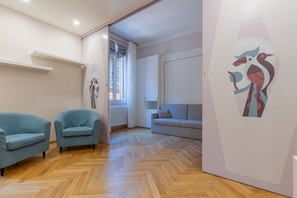 Ein modernes Interieur mit Holzdielen im Fischgrätmuster, zwei blaue Sessel, ein graues Sofa und abstrakte Wandbilder.