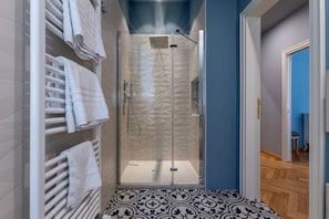 Een badkamer met een glazen douchecabine, witte handdoekhouders, vloertegels met een patroon en een blauwe muur.