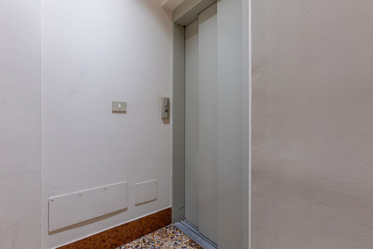 Um corredor estreito com uma porta, um interruptor de luz e uma tomada na parede.