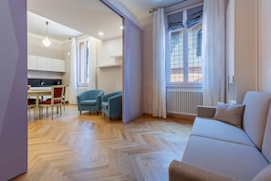 Een moderne woonkamer met een bank, twee fauteuils, een eettafel met stoelen en een keukenhoek.