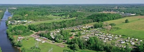 Un camping con vehículos recreativos y remolques, un río y vegetación circundante.