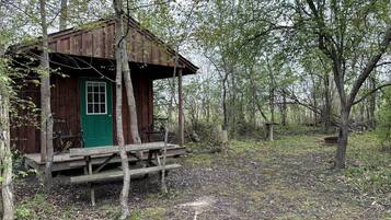 A rustic cabin with a green door, wooden porch, and a bench.