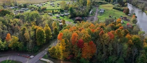 Vista aérea de un camping con vehículos recreativos, un río y follaje otoñal.