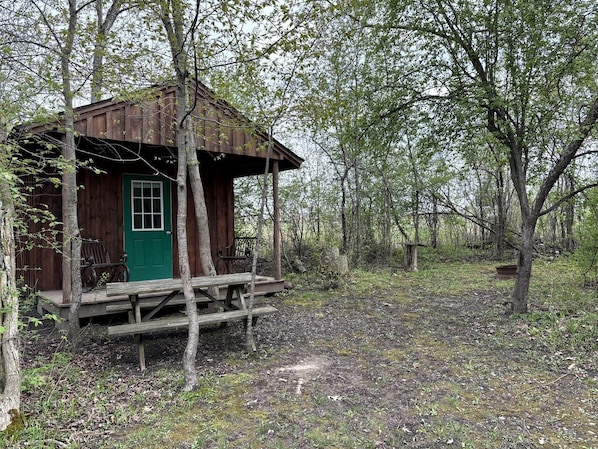 A rustic cabin with a green door, wooden porch, and a bench.