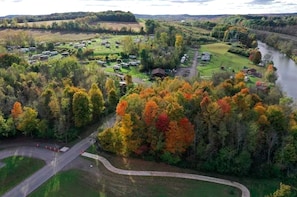 Vista aérea de un camping con vehículos recreativos, un río y follaje otoñal.