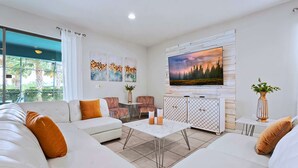 Un salon moderne avec un canapé d’angle, une table basse et un téléviseur fixé au mur, qui est de couleur blanche.