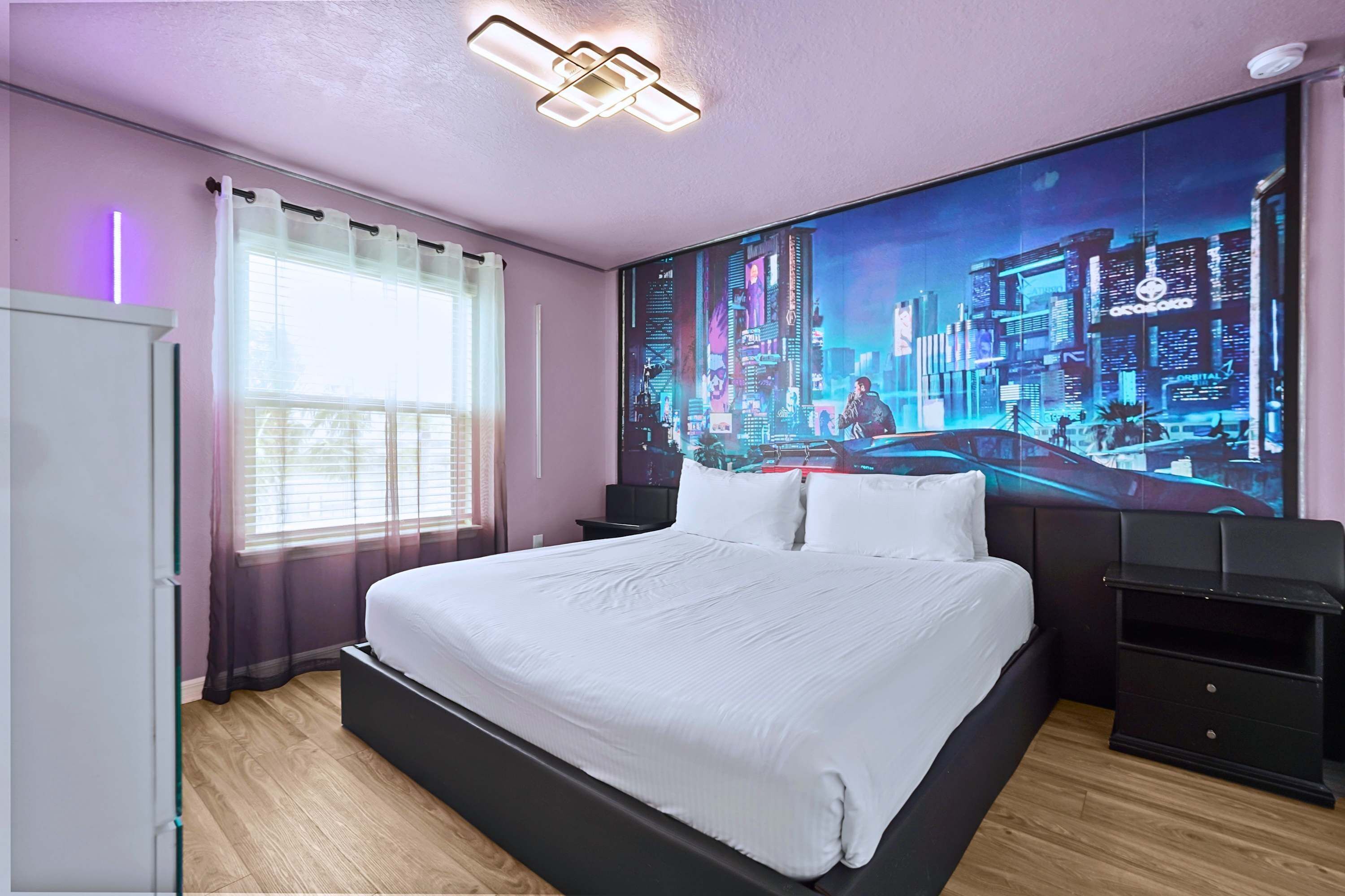 A modern bedroom with a large bed, a cityscape mural, a window with sheer curtains, and a bedside table.