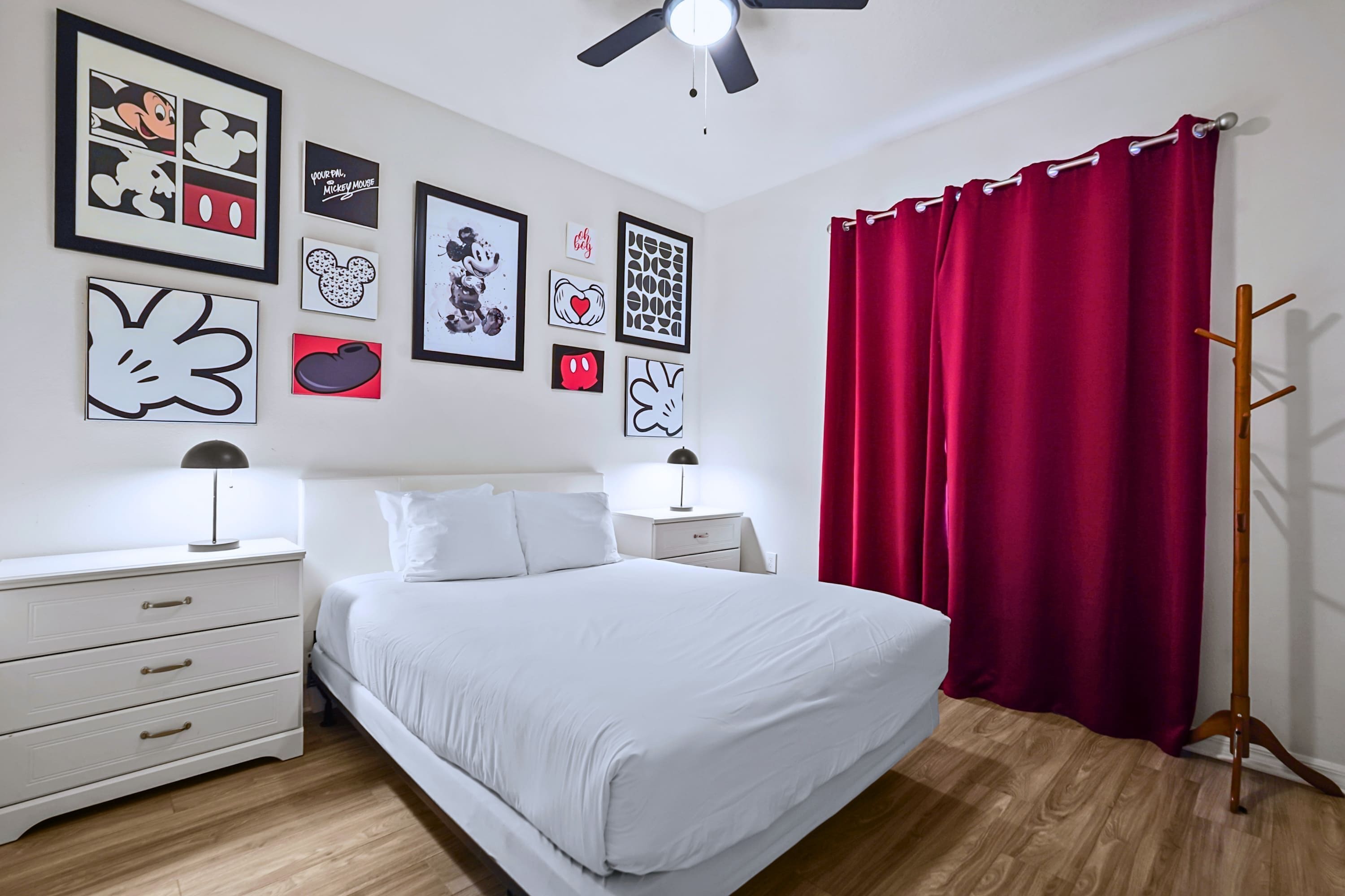 Una camera da letto con un letto, comodini bianchi, una ventola a soffitto e una tenda rossa.