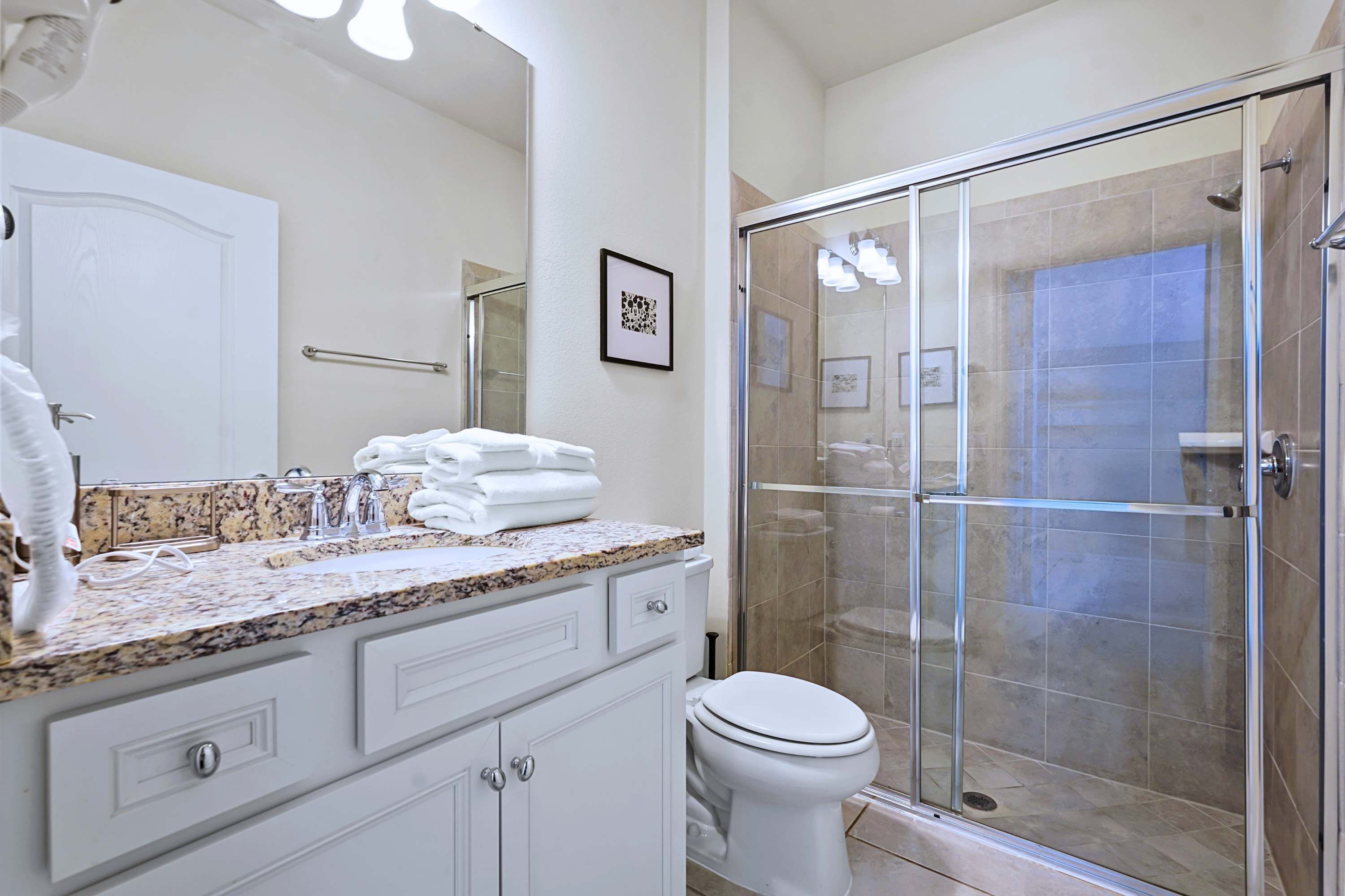 A bathroom with a granite countertop, white cabinetry, a toilet, and a glass-enclosed shower.