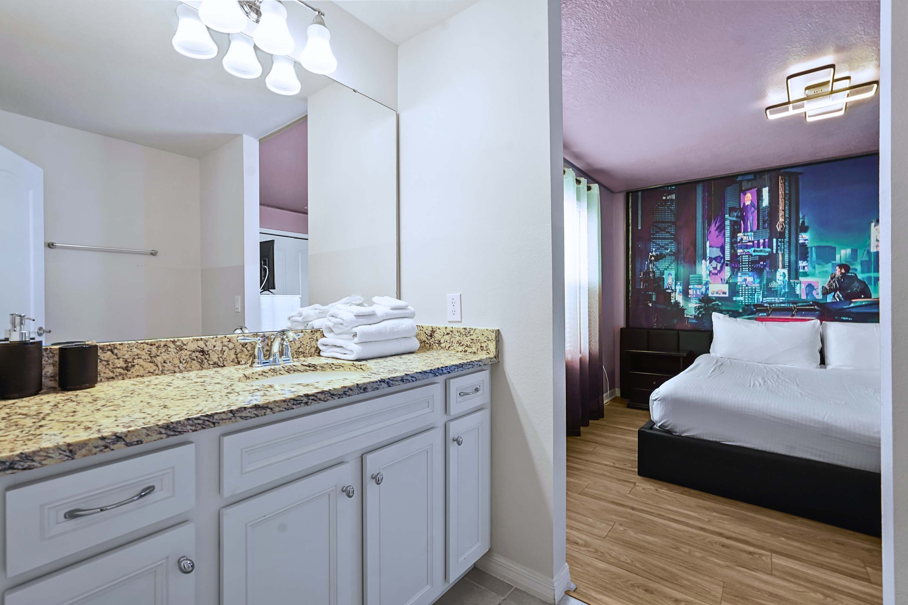 A modern hotel room with a large bed, a bathroom with a granite countertop, and a cityscape mural on the wall.