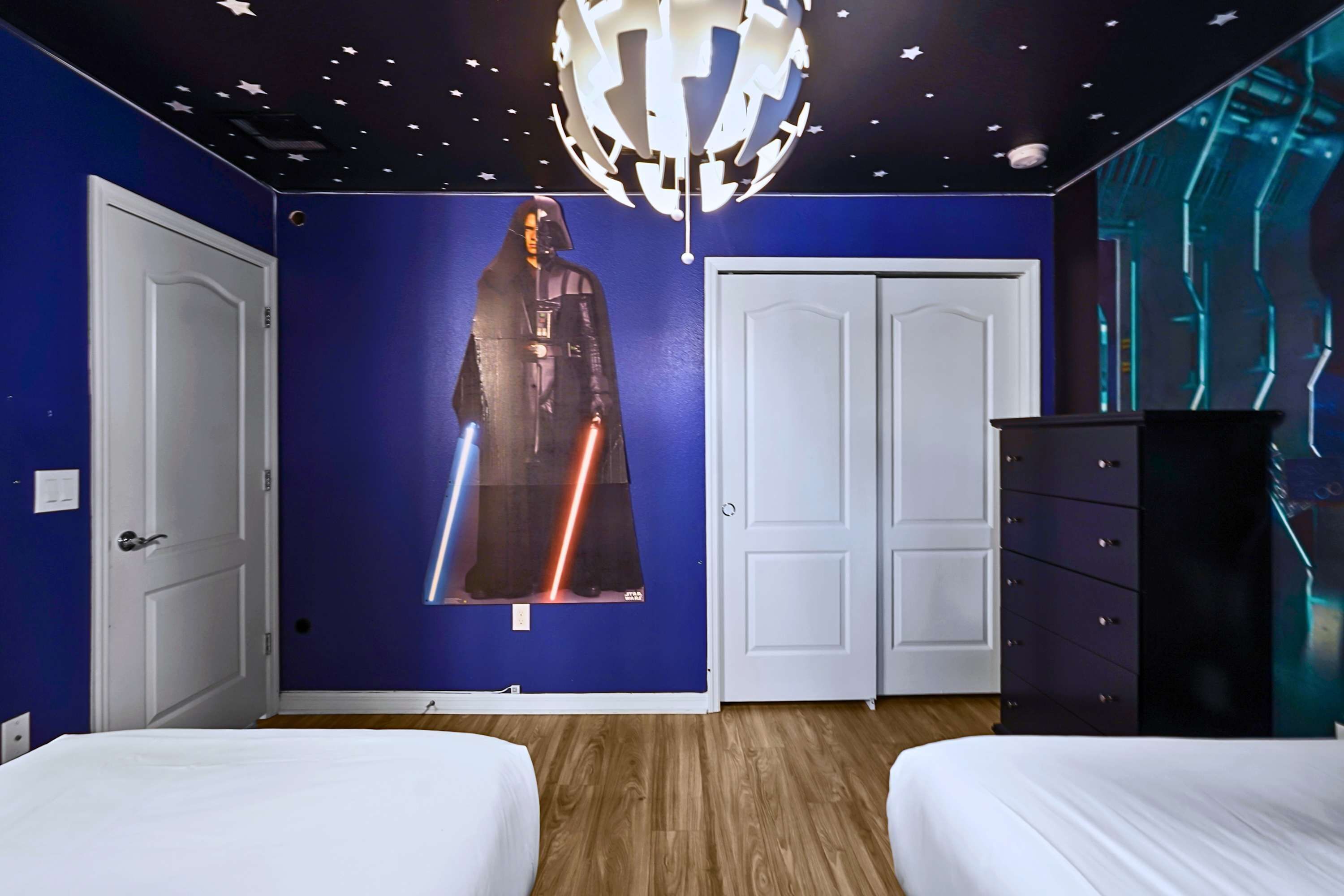 Ein Zimmer mit zwei Betten, einem Kleiderschrank, einer Wand im Stil von Star Wars und einer Deckenleuchte.