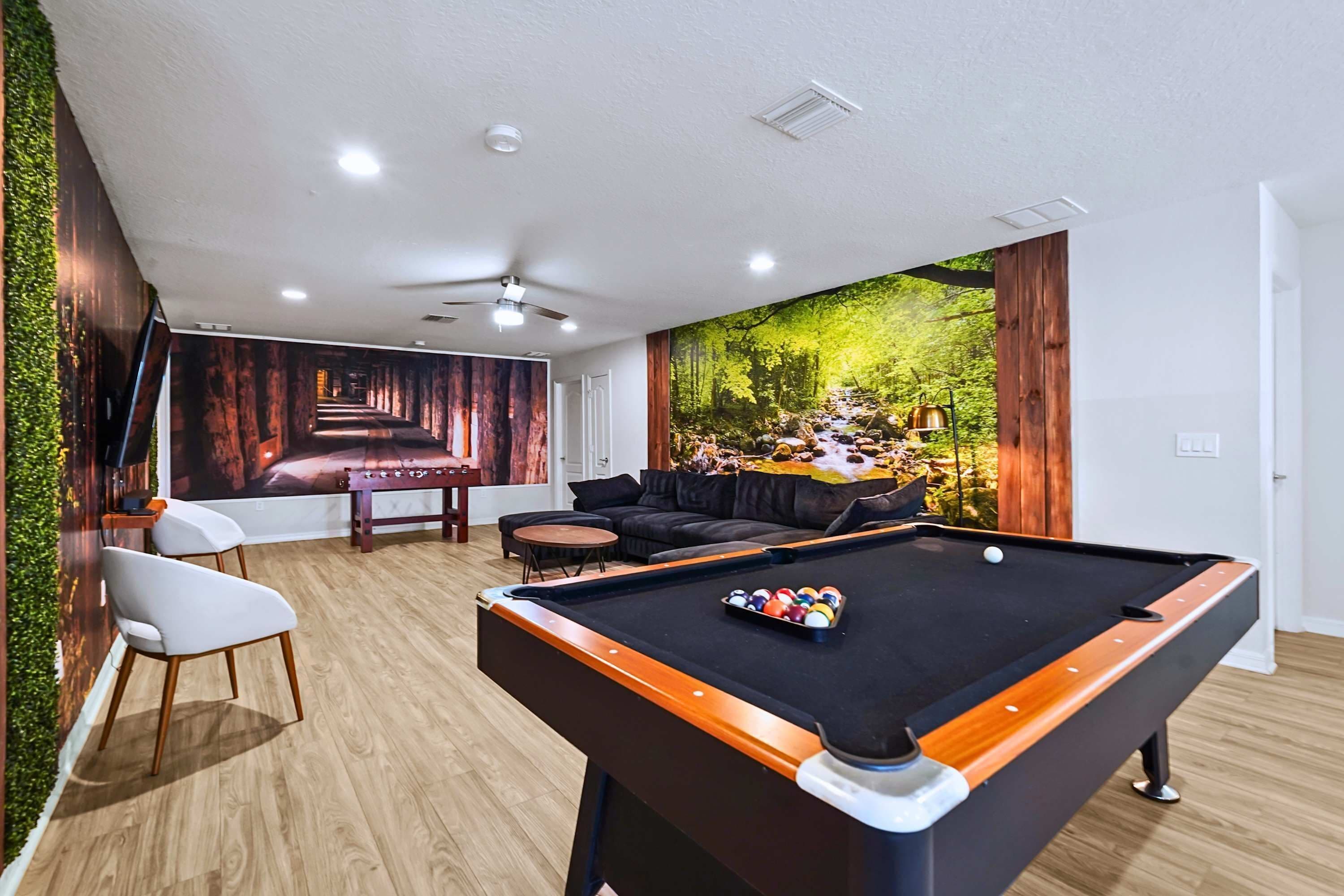 A pool table with balls, a sofa, a chair, and a mural of a forest scene.