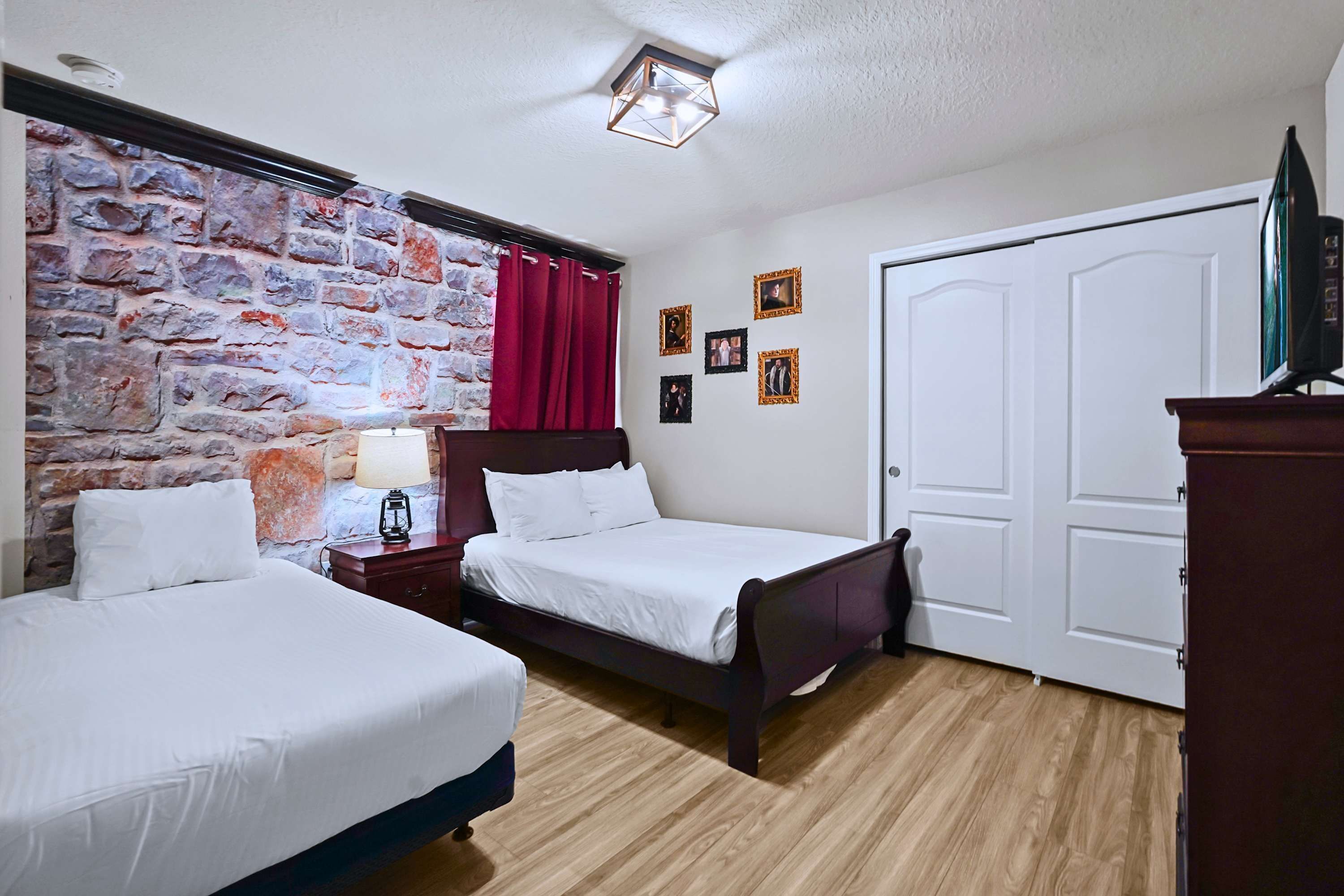 A bedroom with two beds, a stone wall, a red curtain, a wooden floor, and a white door.