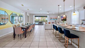 Une cuisine moderne avec un coin repas, comprenant un grand îlot central avec des tabourets, une table à manger avec des chaises et une vue sur l’extérieur.
