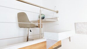 Ein modernes, minimalistisches Zimmer mit weißer Wand, einem Holztisch, einem stuhlförmigen Metallgestell und einem kleinen Regal mit Globus.