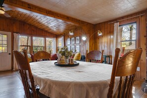 Ein Zimmer mit Holzwänden, einem runden Tisch, Stühlen und einem Fenster mit Vorhängen.