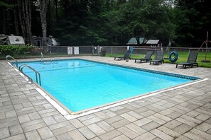 Ein rechteckiger Pool mit Fliesen umrandet, umgeben von einem Zaun und einigen Liegestühlen.