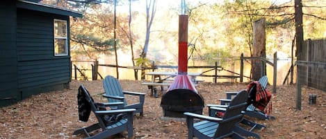 An outdoor seating area with Adirondack chairs, a wood-burning stove, and a picnic table.