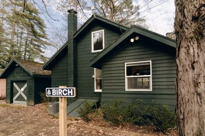 Ein dunkelgrünes Gebäude mit Schornstein, einem Fenster mit zerbrochener Scheibe und einem Schild mit der Aufschrift 'BIRCH'.