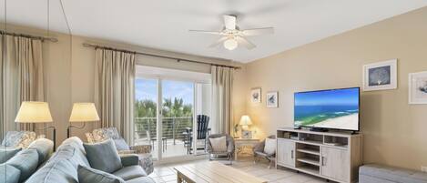 A living room with a sofa, coffee table, TV, and a balcony with curtains.