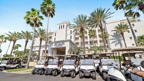 A row of golf carts parked in front of a building with palm trees and a clear sky.