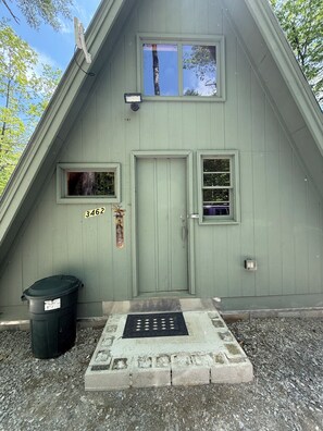 A green-roofed building with a door, two windows, a mailbox, and a trash bin.