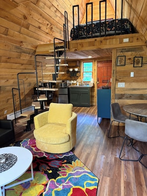 A cozy cabin interior with a loft bedroom, a kitchen, and a dining area.