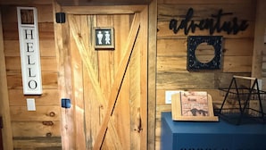 Une porte en bois avec une pancarte indiquant « BONJOUR », une autre indiquant les toilettes pour hommes, et une troisième avec l’inscription « Bienvenue à nos invités », le tout affiché sur le mur.