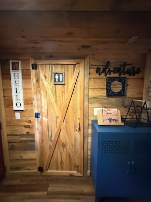 A wooden door with a 'HELLO' sign, a men's restroom sign, and a 'welcome guest' sign on the wall.
