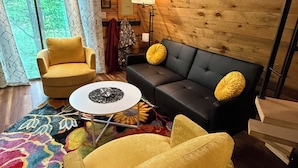 Une pièce chaleureuse avec un plafond en bois, un canapé, un fauteuil jaune, une petite table et un tapis coloré.