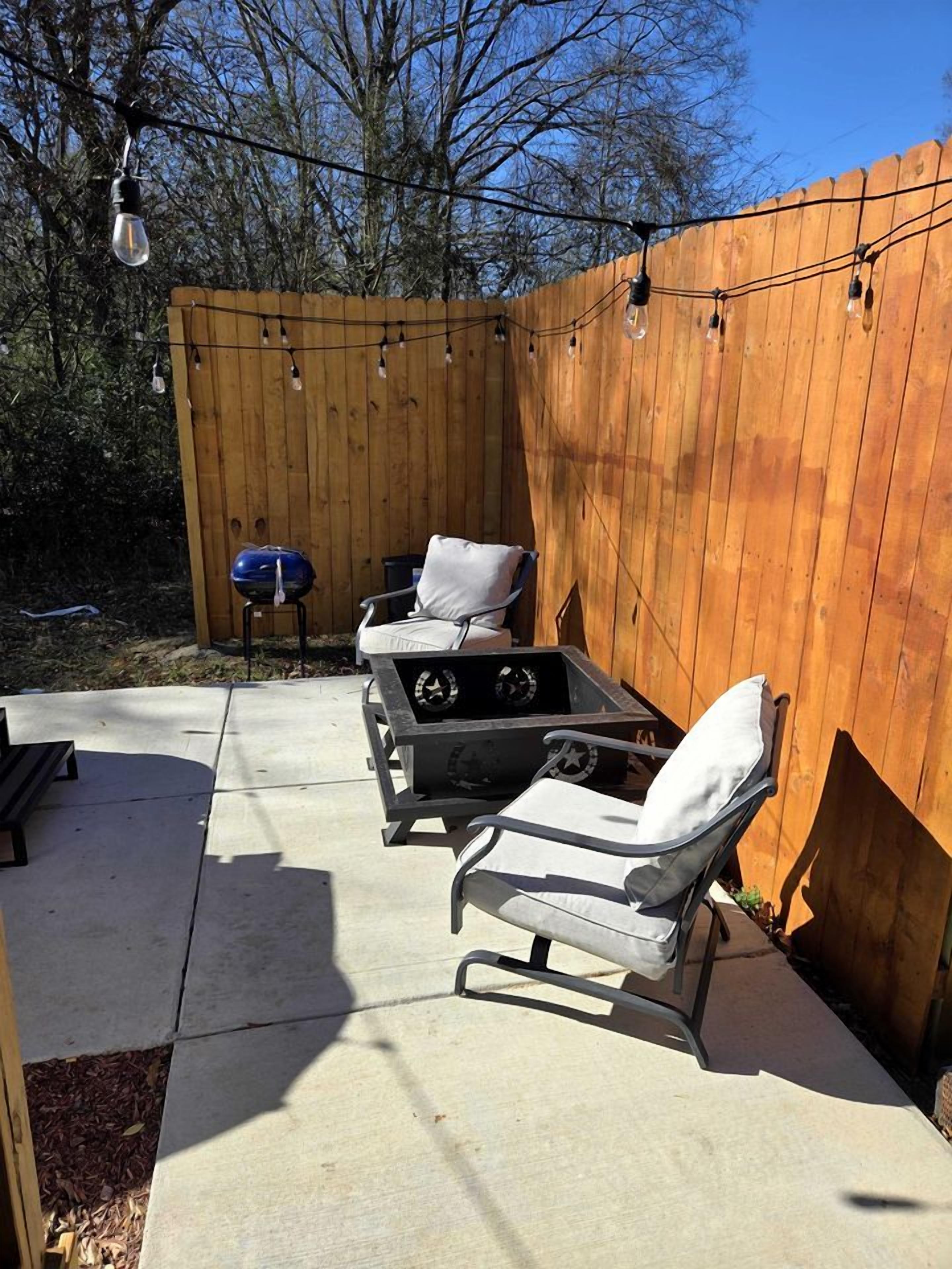 A backyard with a wooden fence, outdoor furniture, a grill, and string lights.