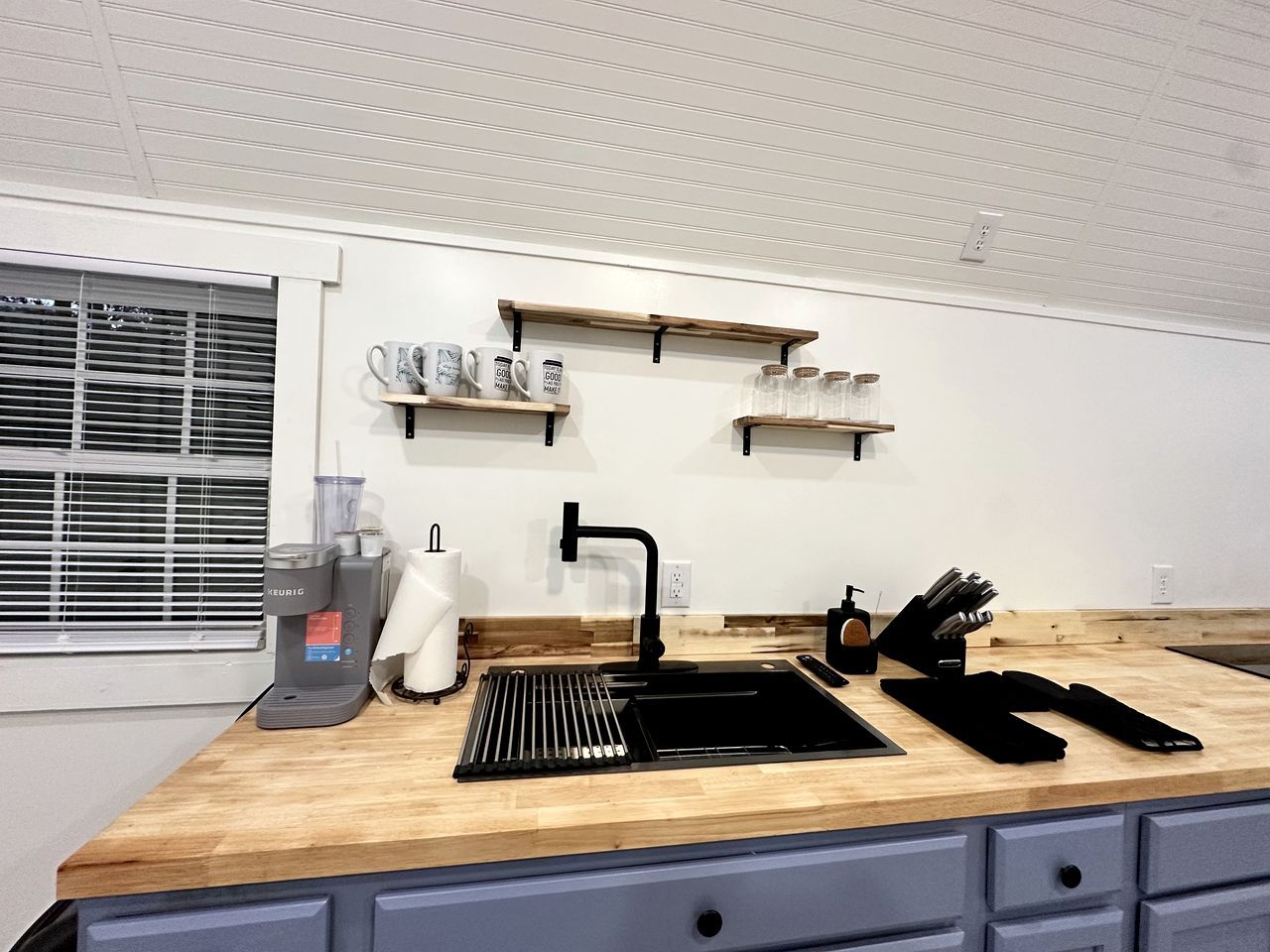 A kitchen with a black sink, wooden countertop, and a coffee maker.