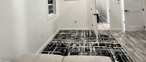A room with a ceiling fan, a mounted TV, a patterned rug, and a door leading to another room.