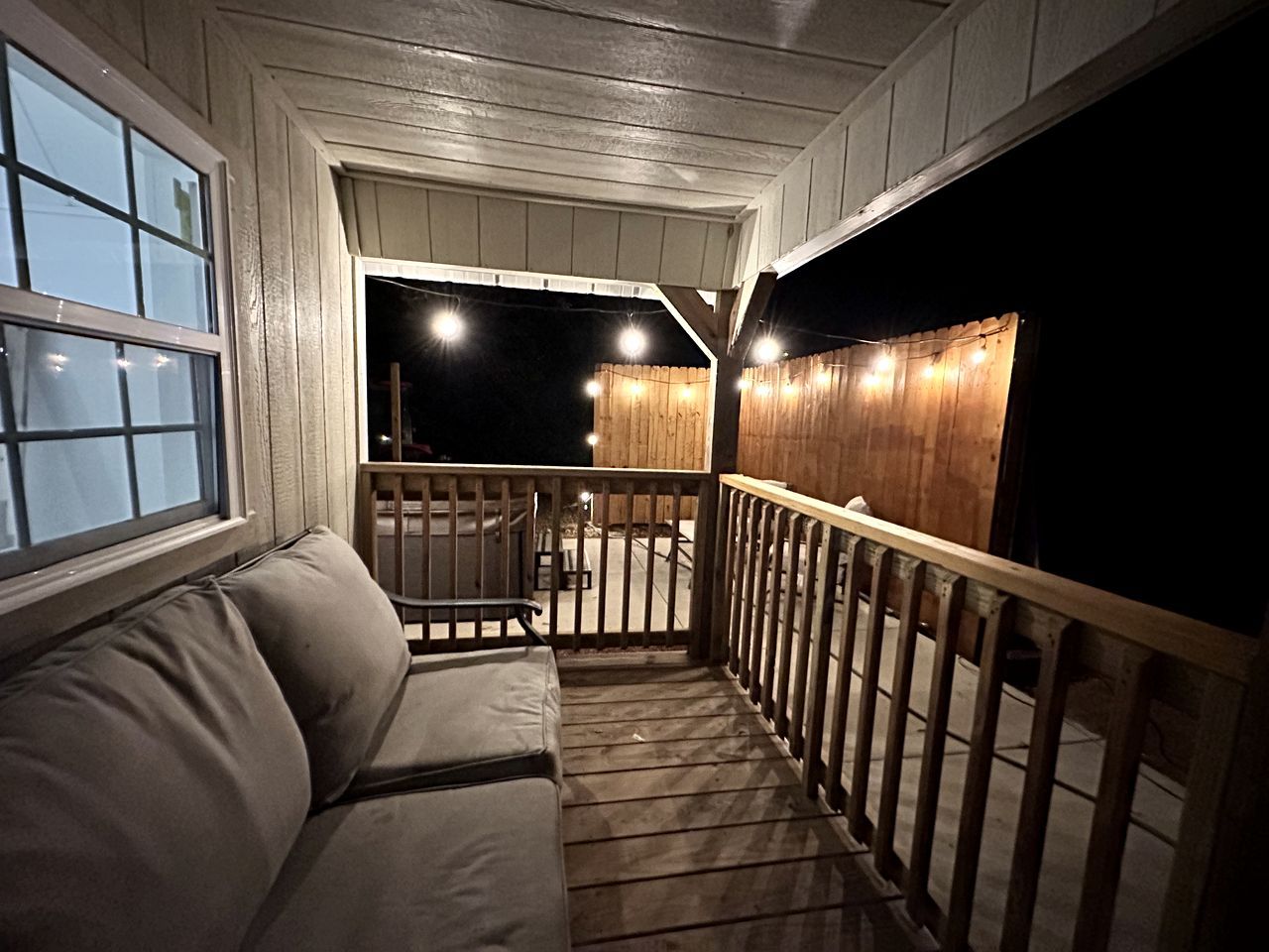 Une véranda couverte avec une balustrade en bois, un banc rembourré et une vue sur l’extérieur la nuit.