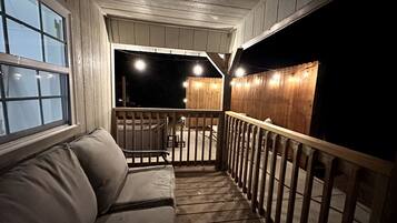 Une véranda couverte avec une balustrade en bois, un banc rembourré et une vue sur l’extérieur la nuit.