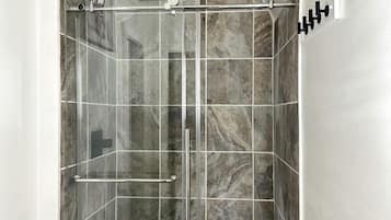 A glass-enclosed shower stall with a white bathtub, marble tiles, and a handrail.
