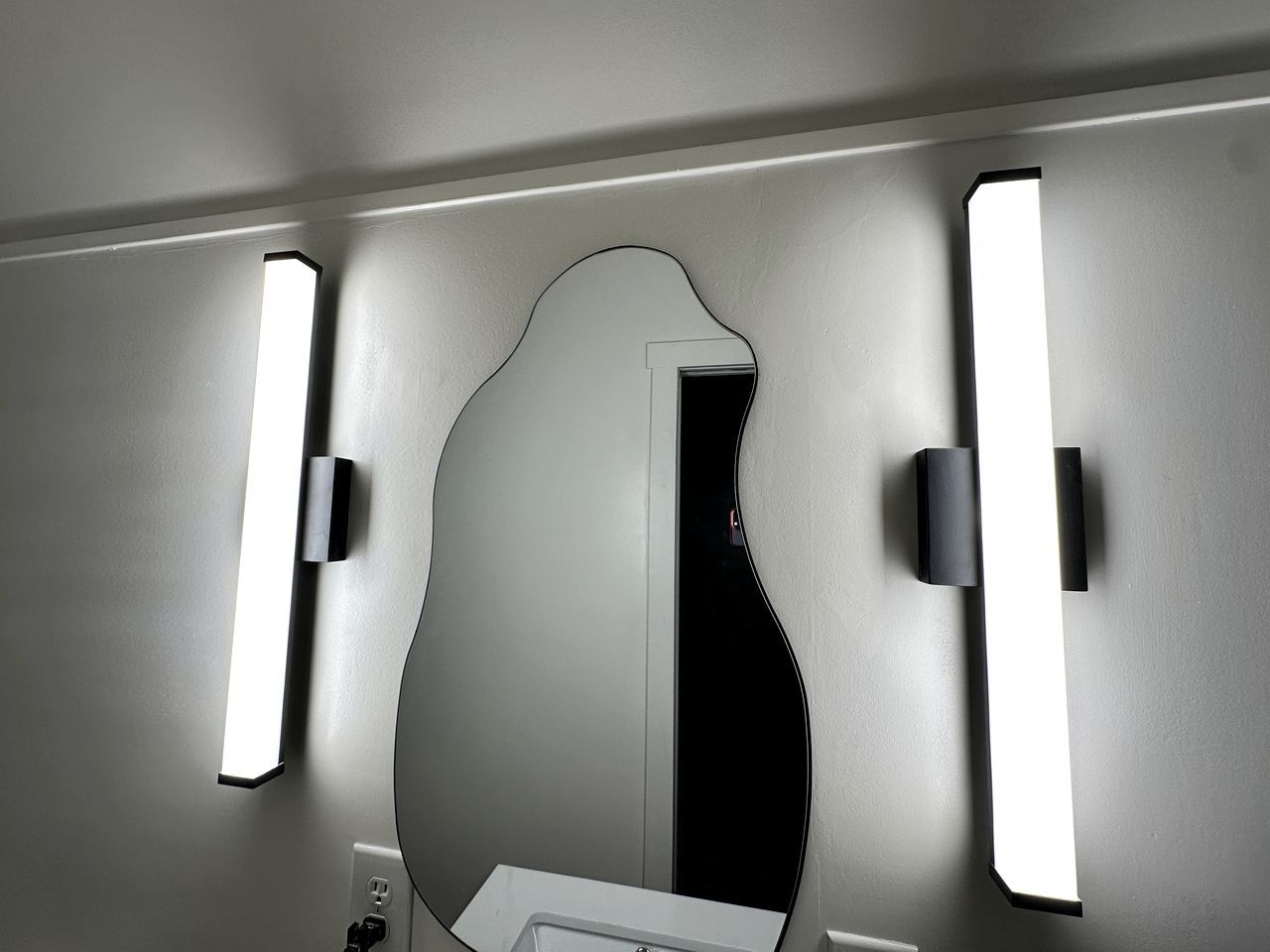 A bathroom with a mirror, two wall-mounted lights, and a door.