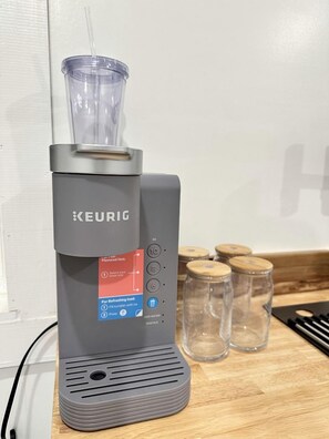 Eine KEURIG-Kaffeemaschine mit Wasserbehälter, Abtropfschale und Bedienfeld mit Tasten für Kaffee, Eistee und Espresso.