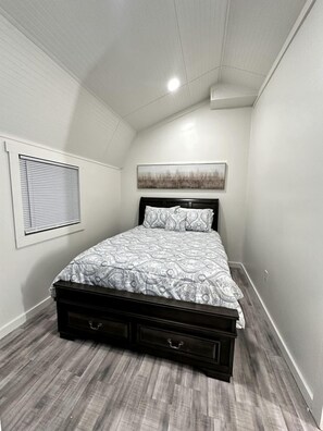 A bedroom with a bed, a window with blinds, a painting on the wall, and a ceiling light. - Rustic Cabin Escape with Hot Tub Near Oxford, Mississippi (Sardis)