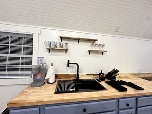 Une cuisine avec un évier noir, un plan de travail en bois et une machine à café.