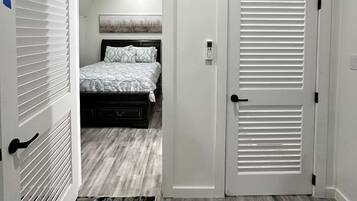 A bedroom with a bed, a white air conditioner, a door with a handle, and a patterned rug.