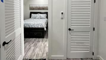 A bedroom with a bed, a white air conditioner, a door with a handle, and a patterned rug.