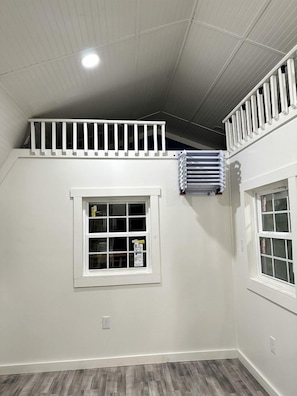 A room with a sloped ceiling, a window with blinds, a radiator, and a white railing on the upper wall.