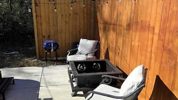 A backyard with a wooden fence, outdoor furniture, a grill, and string lights.