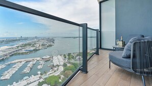 Ein Balkon mit Blick auf einen Yachthafen und die Skyline, eine Couch und ein kleiner Tisch mit Flasche und Glas.