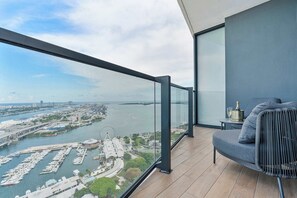 Een balkon met uitzicht op een jachthaven en stadsbeeld, een sofa en een klein tafeltje met een fles en glas.