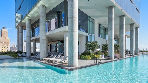 Ein modernes Hotel mit Dachpool, großen Glasfenstern und Blick auf die Skyline der Stadt.