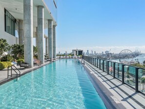 Ein Infinity-Pool auf dem Dach mit klarem, blauem Wasser, umgeben von Liegestühlen und einer Glasufernung.