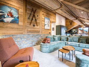 Zona d'estar àmplia amb una paret de pedra, un sofà modular gran i un sostre de fusta.