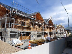 A multi-story building under construction with wooden exterior walls, stone foundation, and metal scaffolding. - Modern apartment, mountain view - 12 guests (La Toussuire)